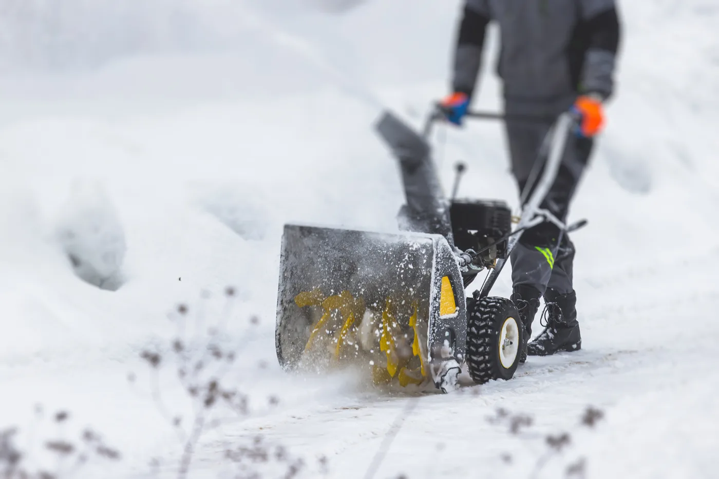 Person clearing a snow-covered driveway with a walk-behind snowblower.